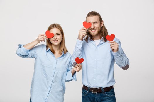 Attractive young in love couple holding red hearts over eyes on white background.