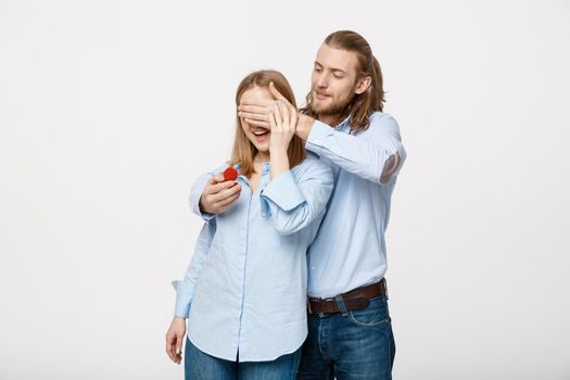 Portrait of handsome beard man hiding his wifes eyes to offer her an engagement ring for a marriage proposal.