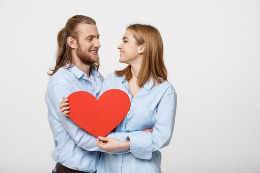 Portrait of happy cute couple in love enjoys Valentine's Day. A man with a beard and a woman with blond short hair holding red heart paper