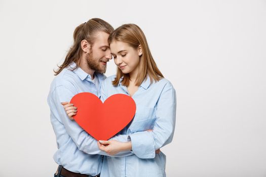 Portrait of happy cute couple in love enjoys Valentine's Day. A man with a beard and a woman with blond short hair holding red heart paper