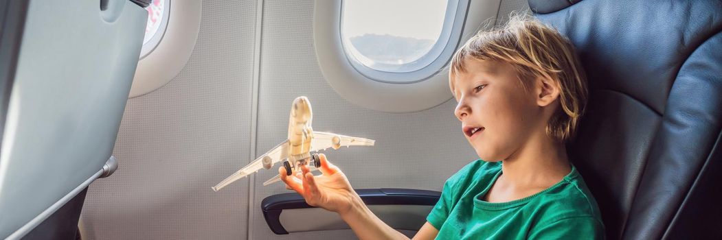 Little boy play with toy plane in the commercial jet airplane flying on vacation. BANNER, LONG FORMAT