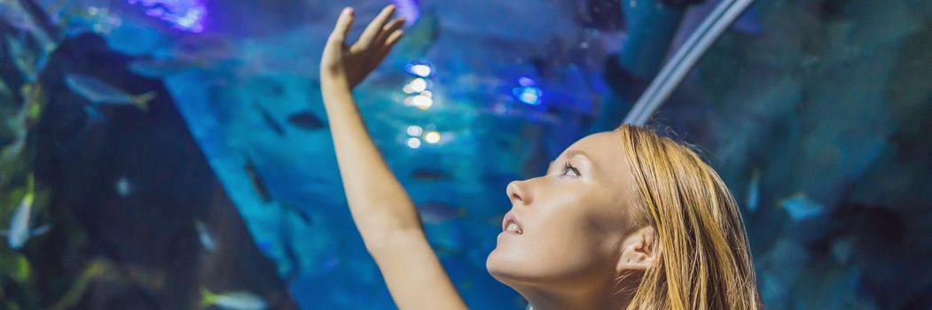 Young woman touches a stingray fish in an oceanarium tunnel. BANNER, LONG FORMAT