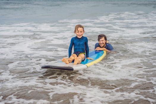 Father or instructor teaching his 5 year old son how to surf in the sea on vacation or holiday. Travel and sports with children concept. Surfing lesson for kids.