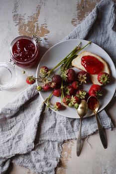 Summer breakfast concept with srawberry jam with bread and fresh harvested berries on gray plate, flat lay, selective focus.