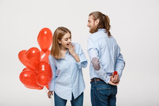 Portrait of Young handsome guy gives a ring to a girl on a white background with red heart air balloons .