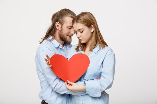 Portrait of happy cute couple in love enjoys Valentine's Day. A man with a beard and a woman with blond short hair holding red heart paper
