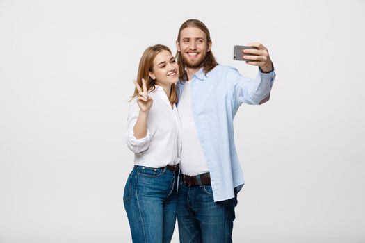 Portrait of a happy couple making selfie photo with smartphone over isolated white studio background