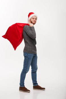 Christmas concept - Young confident smart man holding red big santa bag with a lot of present inside.