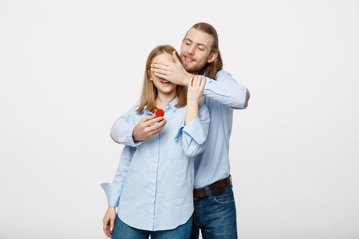 Portrait of handsome beard man hiding his wifes eyes to offer her an engagement ring for a marriage proposal.