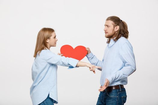 Couple holding heart shape paper with angry facial expression against grey