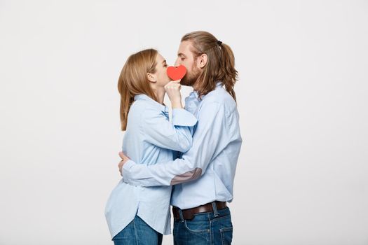 Young attractive couple in blue shirt holding paper heart and kissing