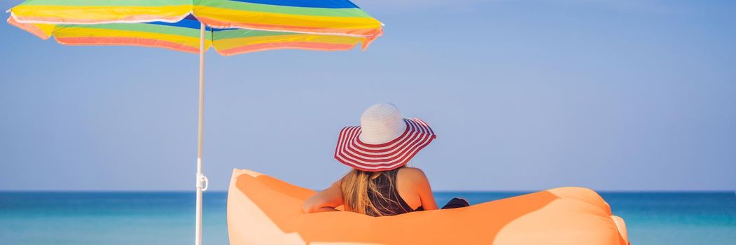 Summer lifestyle portrait of pretty girl sitting on the orange inflatable sofa on the beach of tropical island. Relaxing and enjoying life on air bed. BANNER, LONG FORMAT