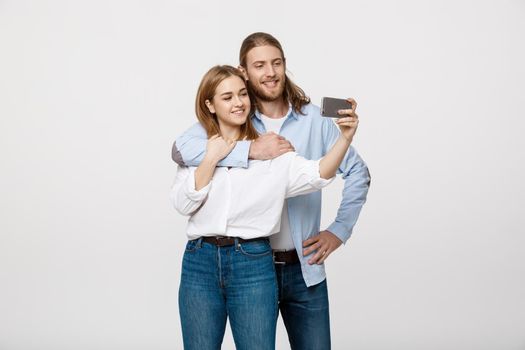 Portrait of a happy couple making selfie photo with smartphone over isolated white studio background