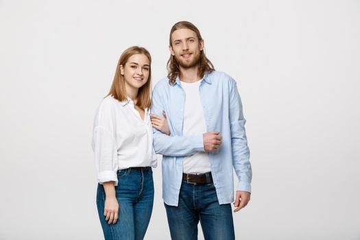 Portrait of attractive young couple smiling for the camera while holding arm to arm. On grey background