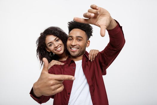 Happy young African American couple looking through a finger frame and smiling while standing isolated on white