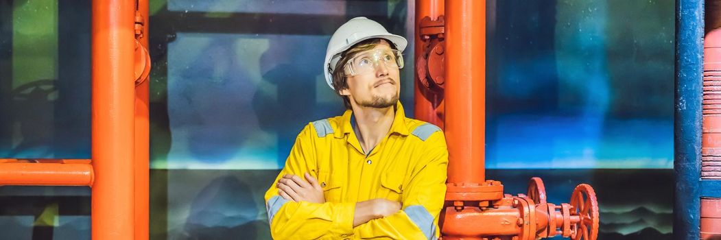 Young man in a yellow work uniform, glasses and helmet in industrial environment,oil Platform or liquefied gas plant. BANNER, LONG FORMAT
