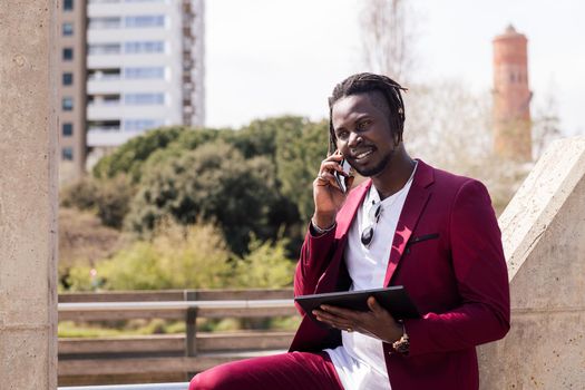 african businessman using a tablet and talking on smart phone outdoors in the city, technology and remote work concept, copy space for text