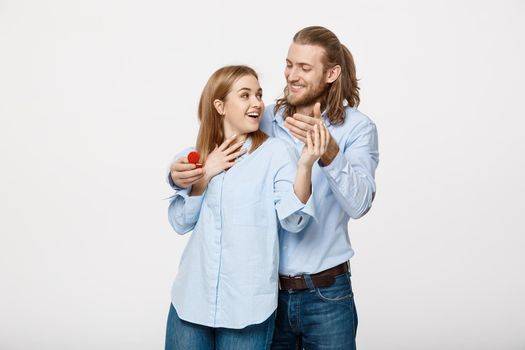 Proposal concept - Portrait of man showing an engagement ring diamond to his beutiful girlfriend over isolated white background .