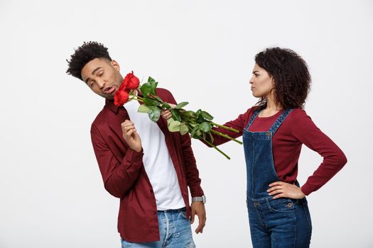 Portrait of a disappointed young woman holding red rose with while standing and angry on her boyfriend isolated over white background.