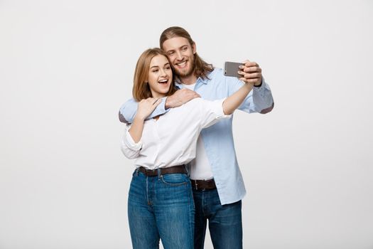 Portrait of a happy couple making selfie photo with smartphone over isolated white studio background