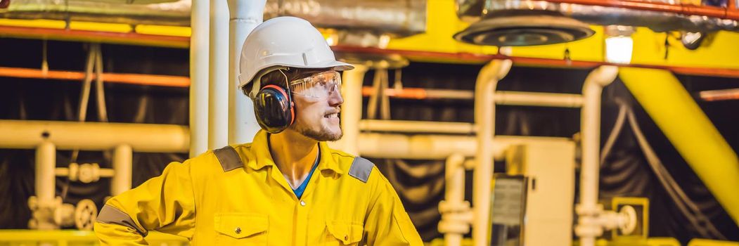 Young man in a yellow work uniform, glasses and helmet in industrial environment,oil Platform or liquefied gas plant. BANNER, LONG FORMAT