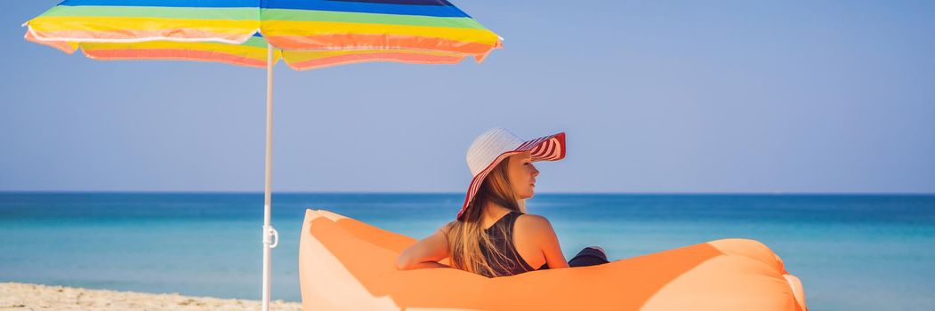 Summer lifestyle portrait of pretty girl sitting on the orange inflatable sofa on the beach of tropical island. Relaxing and enjoying life on air bed. BANNER, LONG FORMAT