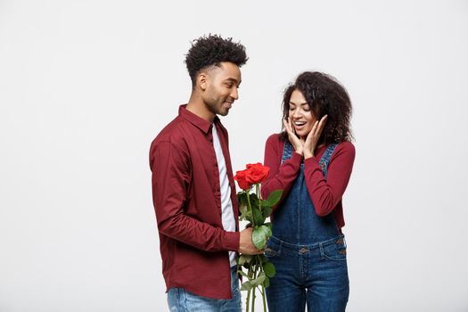 Beautiful elegant couple is hugging and smiling, on gray background. Girl is holding roses.