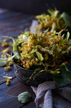 Fresh harvested flowers of linden tree in vintage mental bowl with gray cloth. Linden flowers have the common use in folk medicine. Low key, selective focus.