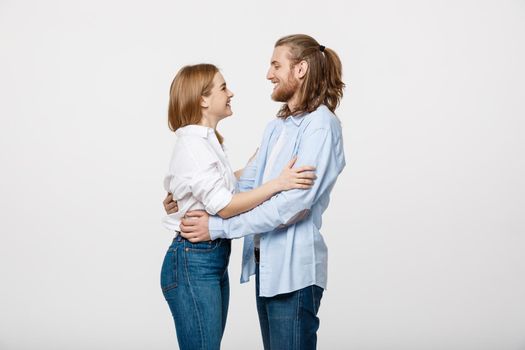 Portrait of cheerful young couple standing and hugging each other on isolated white background.