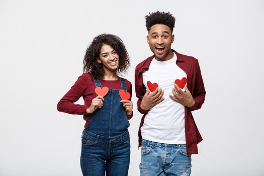 Portrait of african american cheerful couple holding red paper heart enjoy playing standing over grey background.