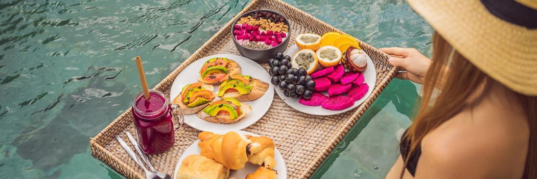 BANNER, LONG FORMAT Breakfast tray in swimming pool, floating breakfast in luxury hotel. Girl relaxing in the pool drinking smoothies and eating fruit plate, smoothie bowl by the hotel pool. Exotic summer diet. Tropical beach lifestyle. Bali Trend.