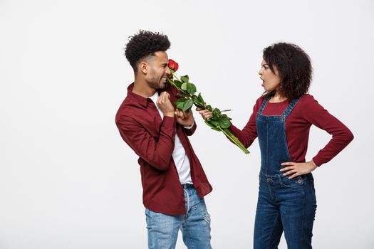 Portrait of a disappointed young woman holding red rose with while standing and angry on her boyfriend isolated over white background.