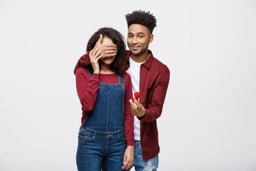 Young handsome African American closing her girlfriend eye and surprising proposal with ring.