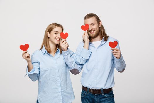 Attractive young in love couple holding red hearts over eyes on white background.
