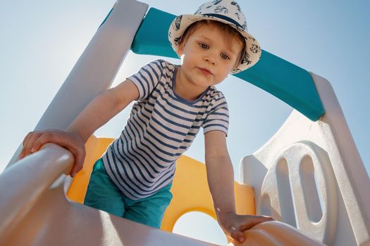 A portrait of a little boy with a striped shirt on top of a slider with a blue sky background behind him