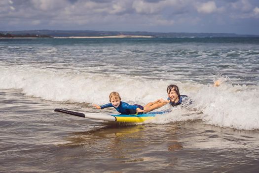 Father or instructor teaching his 5 year old son how to surf in the sea on vacation or holiday. Travel and sports with children concept. Surfing lesson for kids.