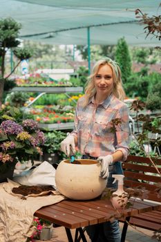 Young woman planting a bush in flower pot using dirt in garden center
