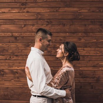 Young couple of lovers man and woman in festive fashionable clothes are hugging. Light casual hairstyle for women with a perm. wood brown plank background