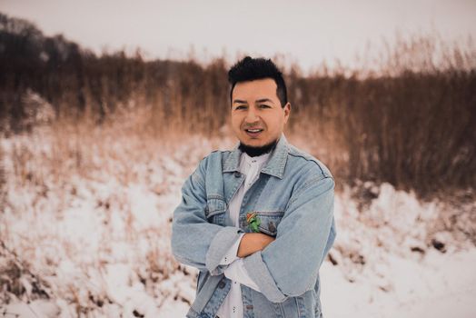 Hispanic brunette man with beard in denim jacket in winter in the middle of snow. Men's Street Fashion Casual Style 2021