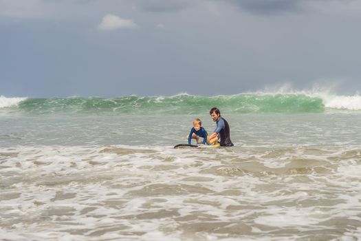 Father or instructor teaching his 5 year old son how to surf in the sea on vacation or holiday. Travel and sports with children concept. Surfing lesson for kids.