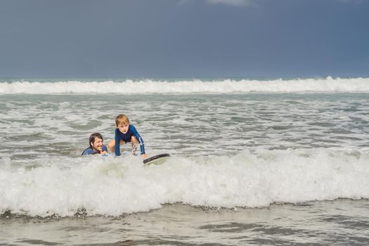 Father or instructor teaching his 5 year old son how to surf in the sea on vacation or holiday. Travel and sports with children concept. Surfing lesson for kids.