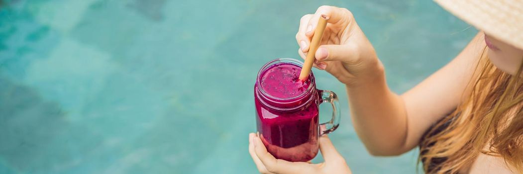 BANNER, LONG FORMAT Young woman drinking Dragon fruit smoothies on the background of the pool. Fruit smoothie - healthy eating concept. Close up of detox smoothie with Dragon fruit.