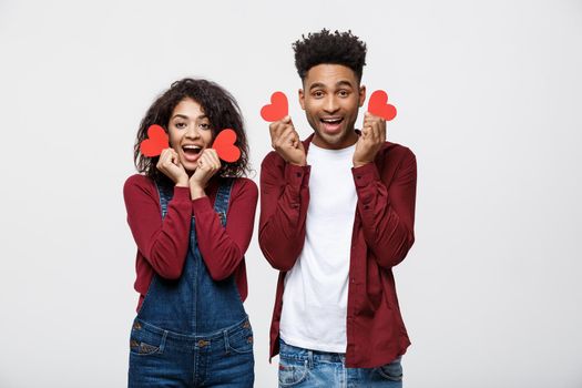 Beautiful Afro American couple holding two red paper heart, looking at camera and smiling, isolated on white background.