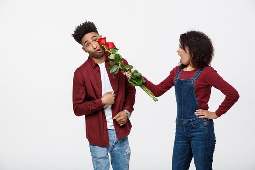 Portrait of a disappointed young woman holding red rose with while standing and angry on her boyfriend isolated over white background.
