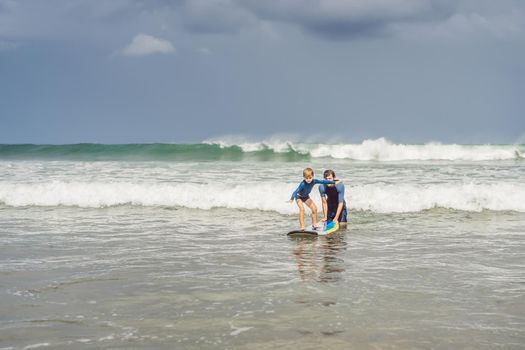 Father or instructor teaching his 5 year old son how to surf in the sea on vacation or holiday. Travel and sports with children concept. Surfing lesson for kids.