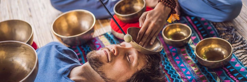 BANNER, LONG FORMAT Nepal Buddha copper singing bowl at spa salon. Young beautiful man doing massage therapy singing bowls in the Spa against a waterfall. Sound therapy, recreation, meditation, healthy lifestyle and body care concept.