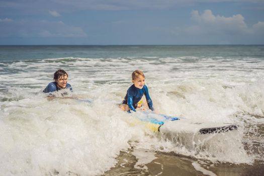 Father or instructor teaching his 5 year old son how to surf in the sea on vacation or holiday. Travel and sports with children concept. Surfing lesson for kids.