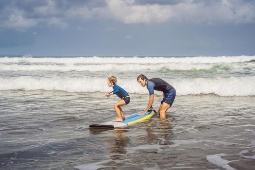 Father or instructor teaching his 5 year old son how to surf in the sea on vacation or holiday. Travel and sports with children concept. Surfing lesson for kids.