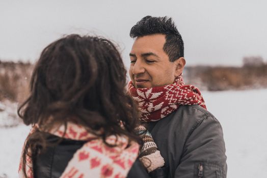young man and woman stand kissing and hugging. bride and groom in love couple in knitted scarf and mittens in winter with snow and snowflakes. wedding dress. mexican people
