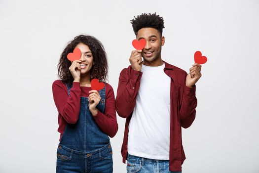 Beautiful Afro American couple holding two red paper heart, looking at camera and smiling, isolated on white background.